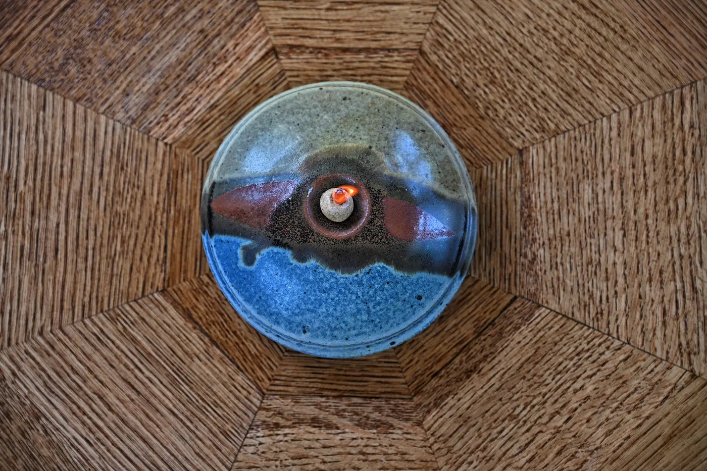 A small flame centered in a round ceramic oil lamp viewed from above
