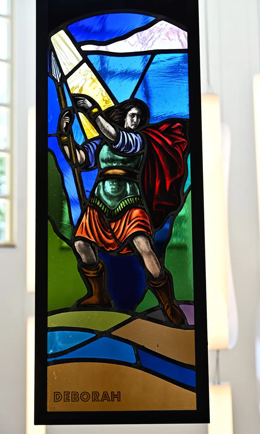 Stained-glass portrait of Deborah raising her hand beneath a beam of light